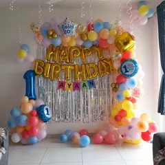 A colorful and cheerful first birthday decoration for a home setting. This setup includes a balloon arch in primary colors against a silver fringe backdrop, with foil number and "Baby Boy" balloons to celebrate the milestone.