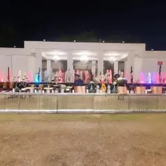 A spectacular night-time buffet setup in front of a large fountain with colorful lights. The long, illuminated counter adds a dramatic and festive feel to this large outdoor wedding reception.