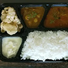 An authentic vegetarian meal box with Gongura Meal Maker curry, Pappucharu (a tangy lentil soup), homemade papads, rice, and curd.