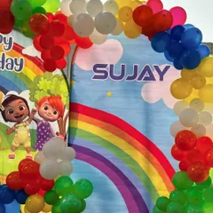 A bright and cheerful Cocomelon-themed first birthday party. The setup features a character backdrop and a rainbow-colored balloon arch.