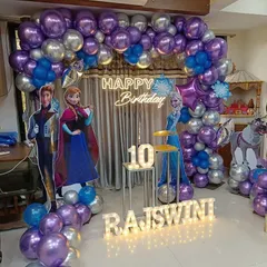 A magical "Frozen" themed 10th birthday party. The decor features a purple and silver balloon arch, character standees of Anna and Elsa, and illuminated marquee letters for the name.