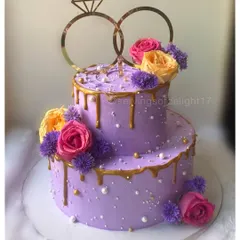A vibrant two-tiered engagement cake in a beautiful purple hue. It's decorated with a gold drip, fresh flowers, and a classic ring topper to celebrate the special moment.
