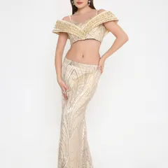 Modern glamour defined. This golden shimmer outfit features a stunning off-shoulder blouse and a sleek fish-cut skirt, perfect for making a statement at a sangeet or reception.