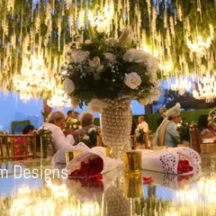 A guest's view of a stunning table centerpiece, with a ceiling of hanging white flowers and lights creating a magical atmosphere. The mirrored table reflects the light, enhancing the sparkle and glamour of the setting.