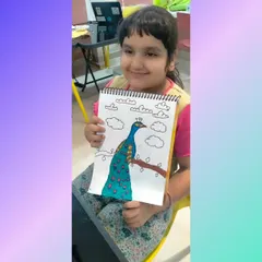 This young artist proudly displays her beautiful peacock drawing. Our drawing classes encourage kids to observe nature and express its beauty through their own colorful creations.