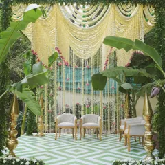 A beautiful stage setup for a South Indian ceremony, featuring a backdrop of draped jasmine garlands. The decor is enriched with banana trees and brass temple toppers, set on a modern geometric-patterned floor for a blend of old and new.