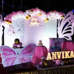 An evening shot of a butterfly-themed birthday for Anvika. The lighting highlights the large butterfly wing props and the personalized marquee name sign, creating a dramatic and enchanting atmosphere for the party.