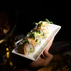A server presents a plate of delicate salmon and avocado sushi rolls. We take pride in offering a wide range of international dishes, all prepared with authentic techniques and the freshest ingredients.