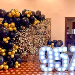 Celebrating academic success with style. This setup for a graduation party features a gold shimmer backdrop, a bold black and gold balloon garland, and large marquee numbers highlighting the student's amazing score.
