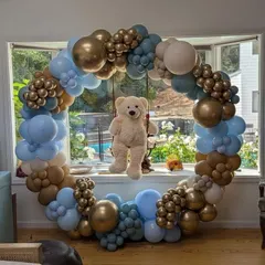 A beautiful teddy bear themed balloon ring set against a window. The arrangement in blue, brown, and gold is perfect for a baby boy's celebration.