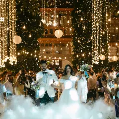 Walking into forever through a magical cascade of lights and ethereal smoke. This is the grand entrance, a moment filled with wonder and the shared excitement of starting a new life together, surrounded by everyone they love.
