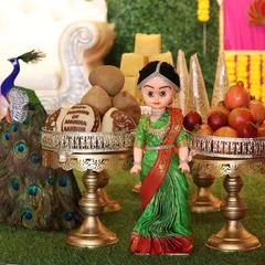 A close up of my seer plate decoration for a baby shower. This arrangement features a doll in a green saree, a peacock figure, and plates holding coconuts, pomegranates, and custom chocolates.