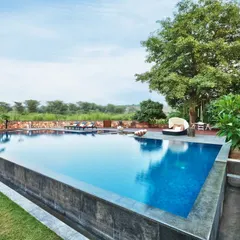 The infinity pool at Aishbagh, designed with a dark stone finish that beautifully reflects the sky and surrounding trees. It serves as the tranquil heart of the property, offering a peaceful escape with views of the Aravalli Hills.