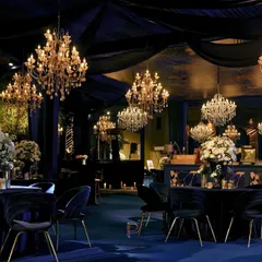 We set a moody and majestic tone for this evening reception with a deep blue and gold color palette. The space is draped in midnight fabrics, with crystal chandeliers casting a warm glow over velvet chairs and tables dressed in white florals.