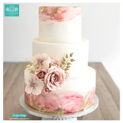 A modern and romantic three-tiered cake featuring a soft pink and gold marble effect. The design is completed with delicate sugar flowers and gold-painted leaves, creating a luxurious look for any grand event.