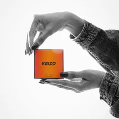 A creative black and white shot with a pop of color, featuring hands framing the "Keizo" product box.