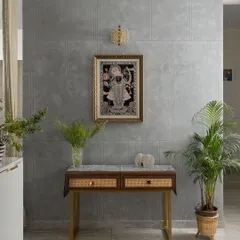 A tranquil corner featuring a traditional Pichwai painting against a modern concrete-finish wall. The simple console table with cane drawers creates a beautiful blend of contemporary design and Indian artistry.