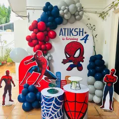 A Spiderman-themed birthday decoration for a 4th birthday party. The setup includes red, blue, and grey balloon arrangements, themed pedestals with web designs, and multiple Spiderman character cutouts.