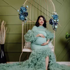 This mom-to-be looks absolutely serene in a mint green mermaid-style maternity gown. The studio setup with the golden birdcage chair and floral decor creates a beautiful, elegant portrait.