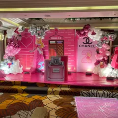 We brought a little girl's fashion-themed dream to life with this vibrant pink stage for her second birthday. The backdrop includes custom elements like a Chanel logo, a princess cutout, and perfume bottle props, making it a perfect photo opportunity.