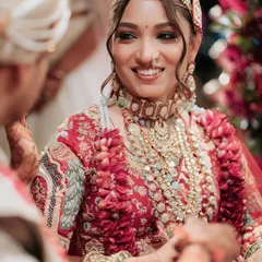 A candid moment of love and laughter during the wedding ceremony. The bride's radiant makeup, with soft waves in her hair, looks stunning with her intricately embroidered red lehenga.