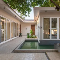 A daytime view of the central courtyard at The Amberle resort in Yelagiri. The design uses large glass windows and doors to connect the interior spaces directly with the serene outdoor pool and walkway.