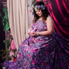 A tender moment captured during a fantasy-themed shoot. The mom-to-be, dressed in a floral gown, cradles a pair of tiny baby shoes, lost in a moment of quiet reflection.