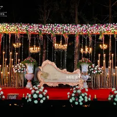 A full view of a regal reception stage setup. The combination of a rich red carpet, a classic chaise lounge, intricate floral arches, and warm chandelier lighting creates an atmosphere of pure opulence and romance for your grand evening.