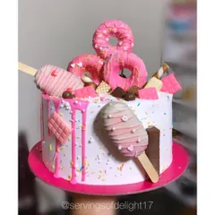 A cake that looks like it came straight from Candyland! This fun drip cake is decorated with pink donuts, cakesicles, chocolate bars, and lots of sprinkles.
