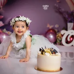 Crawling towards her first birthday cake! This little princess, surrounded by soft purple and green florals, is ready for her sweet celebration.