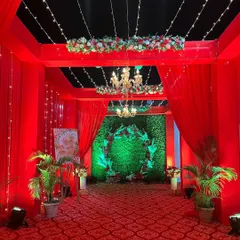 A dramatic red-draped entrance tunnel leading to a greenery photo wall. The contrast between the red fabric and the green backdrop creates a bold and inviting entryway.
