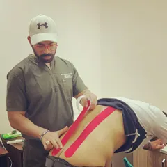 I am applying kinesio tape to a client's lower back. This elastic tape provides support and stability to muscles and joints without restricting range of motion, making it ideal for pain relief during travel or activity.