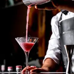 A vibrant pink cocktail being poured into a classic martini glass. We love creating visually stunning drinks that taste as good as they look, perfect for any celebration.