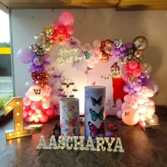 A magical butterfly-themed first birthday with a photo backdrop, a purple and pink balloon arch, and a light-up '1'.