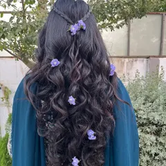 Turn heads with a hairstyle as beautiful as you. This look features long, flowing waves with a simple braid and scattered purple flowers for a touch of fairytale magic.