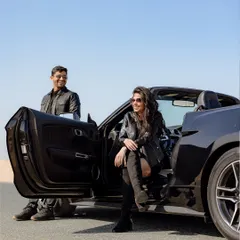A cool, stylish portrait of the couple with their convertible in the Dubai desert, capturing a high-fashion, adventurous vibe.