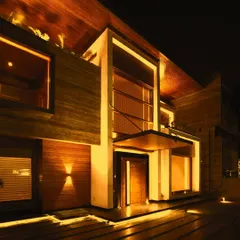This is the entrance to the 'Kohinoor' residence, a project where light was used to enhance the natural warmth of the stone and wood. The design employs a combination of recessed linear lighting, subtle uplights, and focused downlights to create an inviting and luxurious welcome.
