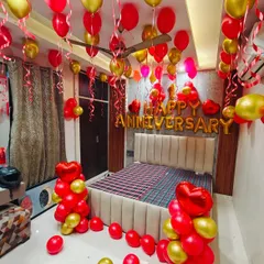 A classic anniversary room decoration in red and gold. The room is filled with balloons floating to the ceiling, balloon bouquets, and a large "HAPPY ANNIVERSARY" foil banner above the bed to surprise your loved one.