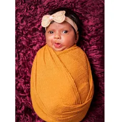 A simple and adorable portrait of a swaddled newborn with a funny expression. This shot captures the quirky and cute personality of a new baby against a rich, textured background.
