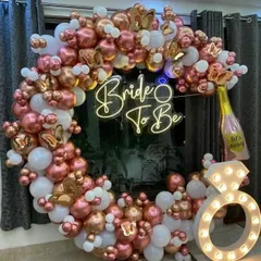 A glamorous 'Bride To Be' setup with a circular balloon arch in rose gold and white, a neon sign, and a light-up diamond ring prop.