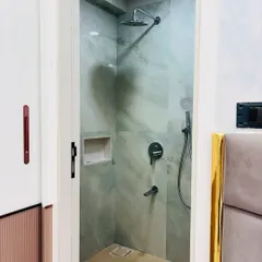 A view into the shower area, which is separated by a frameless glass door. The walls are clad in light green marble-finish tiles, creating a serene and calming atmosphere.
