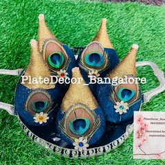 A set of five coconuts decorated with royal blue velvet, gold thread, and natural peacock feathers, presented in a silver tray for an auspicious occasion.