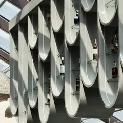 A daytime shot of the suspended bar display highlights its unique form and the way it interacts with sunlight. The design turns bottle storage into an art installation, visible from all angles of the restaurant.