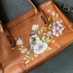 A still shot of the custom hand-painted Gucci bag, showing the delicate details of the bird and pink flowers on the brown leather.