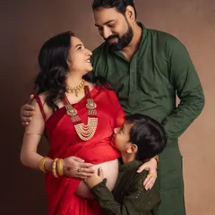 A moment of quiet connection before the family grows. I love how the traditional red saree and jewelry add such elegance to this maternity portrait, while her son's gentle kiss on the baby bump tells a story of love and anticipation.