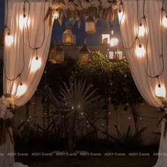 A dreamy bohemian arch, perfect for a photo backdrop or ceremony space. The design features soft white drapes, hanging lanterns, Edison bulbs, and delicate floral accents for a rustic yet elegant feel.