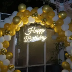 A close-up of a "Happy Birthday" neon sign surrounded by a gold and white balloon arch. We capture the festive details of your event.