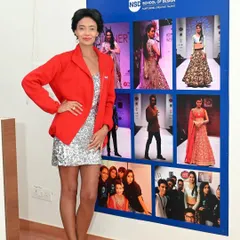 A staff member from the International School of Design posing next to a display of student work. This visually connects the institution's leadership to its creative output.