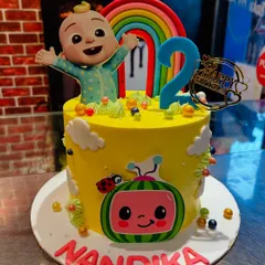 A sunny yellow Cocomelon cake for Nandika's second birthday, topped with a happy JJ and a bright rainbow.