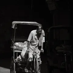A cycle rickshaw puller pedals through a dark lane in Old Delhi, a slice of light illuminating his daily toil.